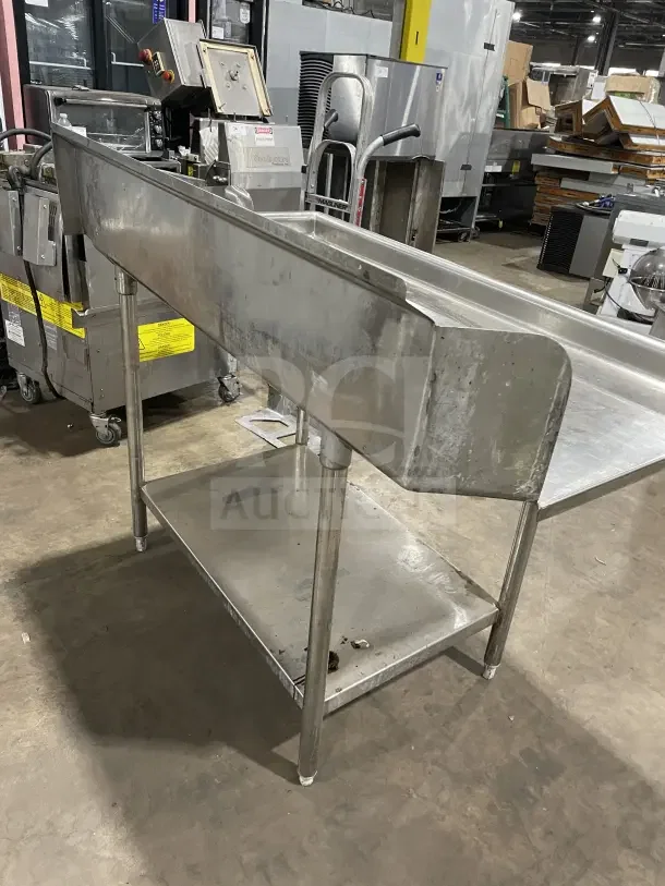 Commercial stainless steel dishtable with backsplash on casters, showing signs of use. Includes lower shelf for storage.