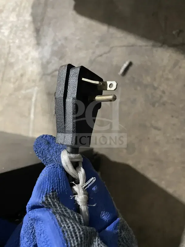 Power plug of a commercial open-air merchandiser refrigerator, showing three-prong design and secure cable knot.