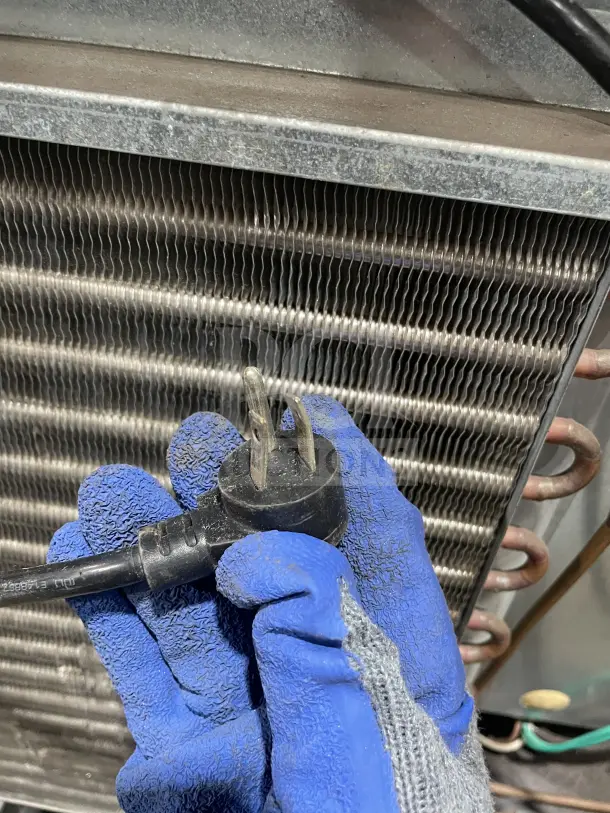 Gloved hands holding a plug in front of a metallic coil, related to Delfield Enodis Series refrigerator.