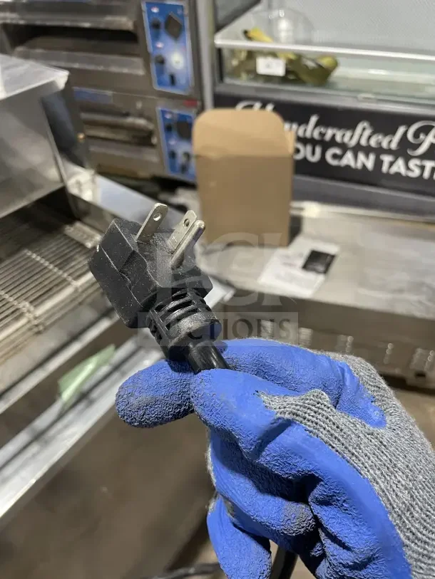 Avantco TTP14240 stainless steel countertop conveyor pizza oven plug, held by a gloved hand.
