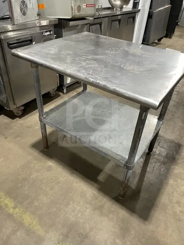 Commercial stainless steel equipment stand with two compartments, on legs. Shows wear; suitable for kitchen use.