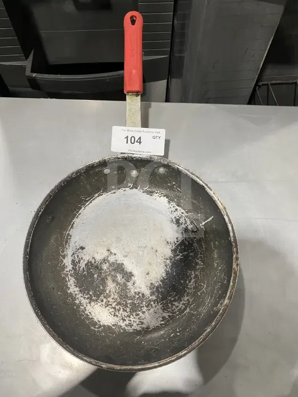 Commercial aluminum non-stick fry pan with wear, featuring removable red silicone sleeve. Auction label displays "104 QTY".