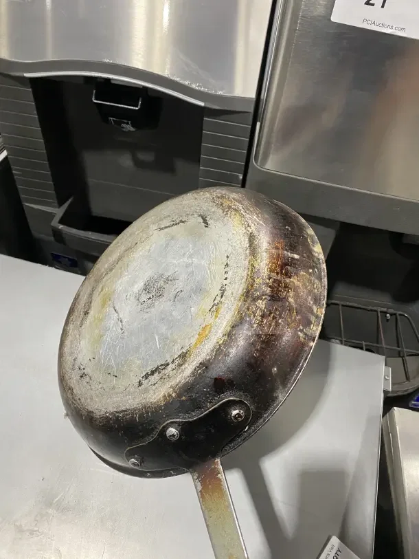 Commercial aluminum non-stick fry pan with wear and patina, featuring a removable red silicone sleeve.