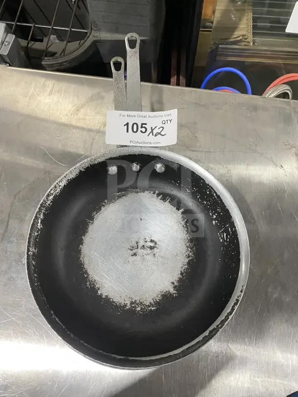 Non-stick aluminum fry pans with handles, commercial use, visibly worn, auction tag "105 x2" indicating double bid offer.