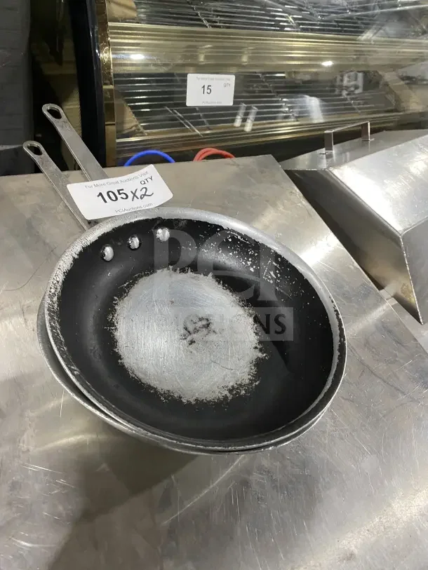 Two commercial aluminum non-stick fry pans with handles, visibly worn condition, auction label reads "105 x2."