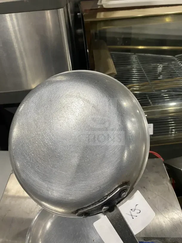 Commercial aluminum non-stick fry pan, metallic finish, attached handle, visible scuff marks, paper tag labeled "XS."