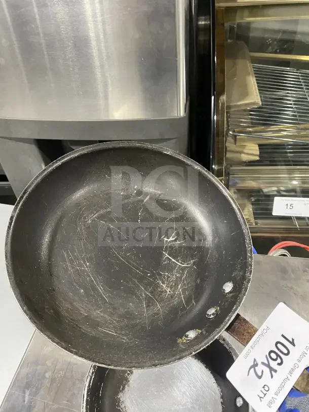 Commercial aluminum non-stick fry pan with handle, used condition with visible scratches; auction lot tag "106x2" attached.