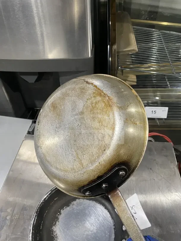 Commercial aluminum non-stick fry pans with handles, showing signs of use and wear. Suitable for industrial kitchens.