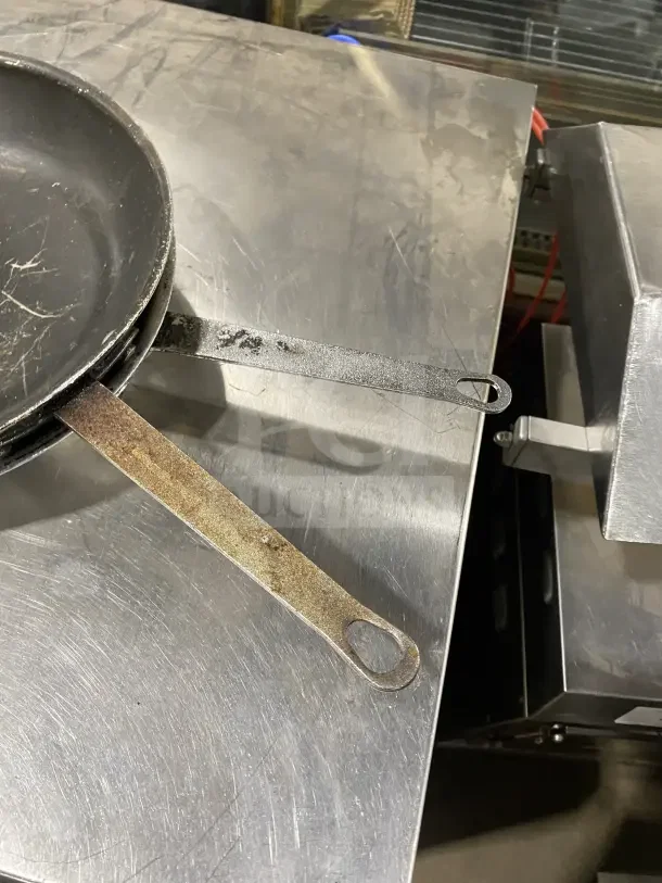 Commercial aluminum non-stick fry pans with handles, visible wear, durable material, suitable for professional kitchens.