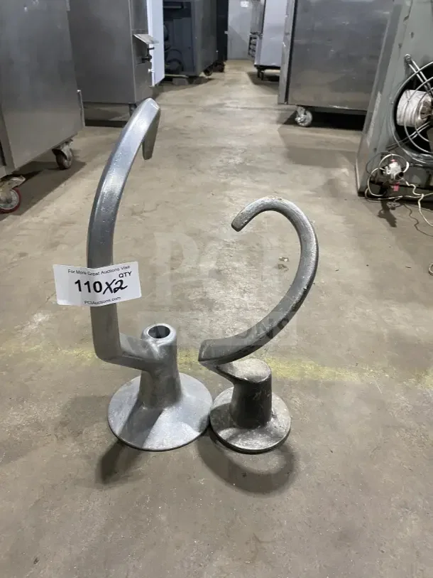 Commercial stainless steel spiral dough hooks in industrial setting, labeled "110X2," showing two hooks, used condition.