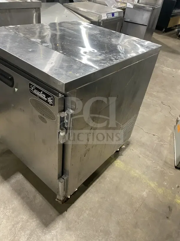 Leader stainless steel single-door undercounter refrigerator on casters, with poly-coated wire rack. Some surface wear visible.