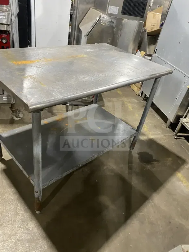 Commercial stainless steel utility stand with two compartments. Features a durable surface and storage shelf. Visible wear and rust.