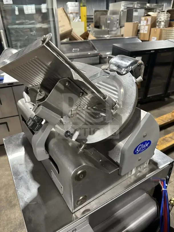 Chefmate Globe Series stainless steel deli meat slicer on legs, electric powered, manual gravity feed, in a commercial setting.