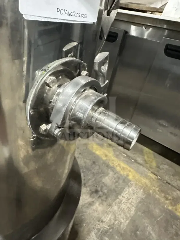 Stainless steel industrial tank with a hose connector and visible auction tag. Appears in used condition.