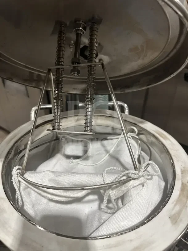 Stainless steel brewing vessel with open lid, showing interior springs and a fabric filter bag. Appears in used condition.
