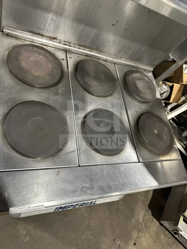 Imperial stainless steel 6-burner electric hot plate range with backsplash, overhead salamander shelf, and wired oven rack.
