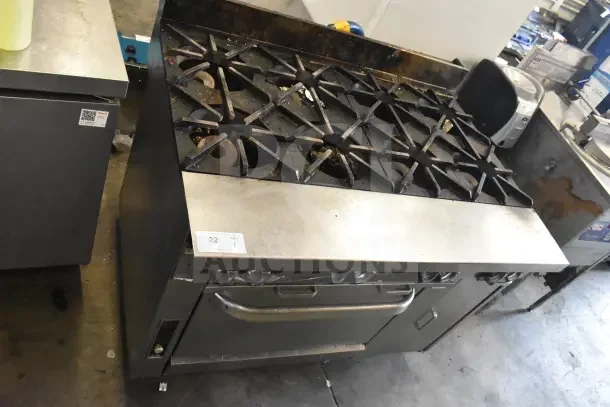 Commercial gas-powered 8 burner range with oven, used condition, on commercial casters, visible wear, numbered tag present.