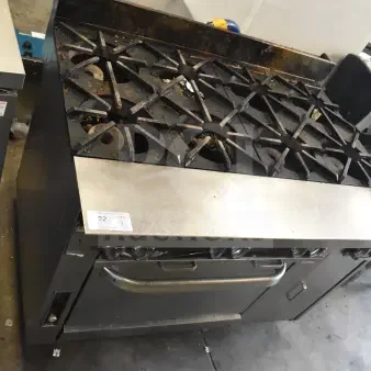 Commercial gas-powered 8 burner range with oven, used condition, on commercial casters, visible wear, numbered tag present.