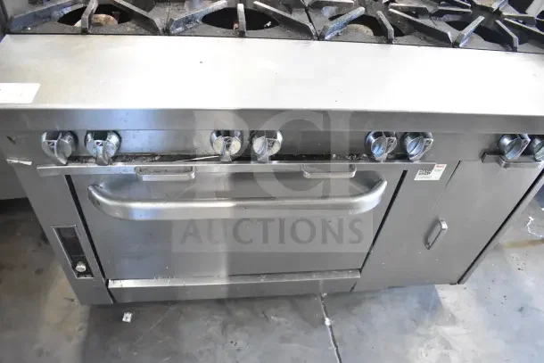 Commercial gas-powered 8 burner range with oven on casters, stainless steel, visible wear, robust knobs, attached label.