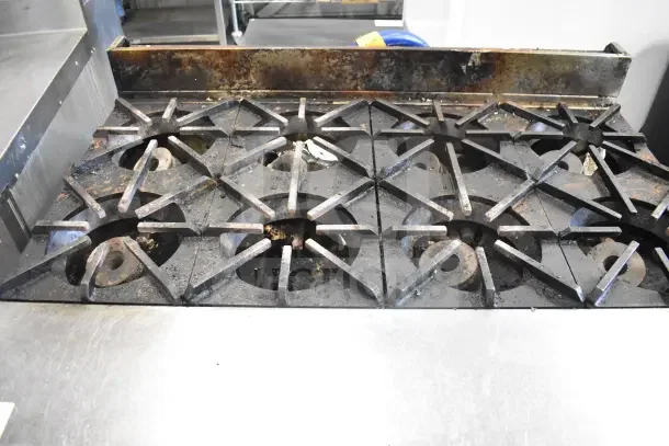 Commercial gas-powered 8 burner range with oven, visible wear, on commercial casters, ideal for professional kitchens.