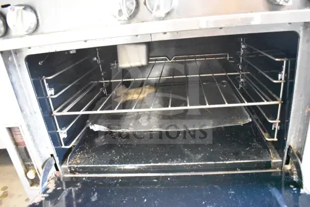 Commercial gas-powered 8 burner range with oven, featuring commercial casters. Visible interior and knobs, moderate wear.
