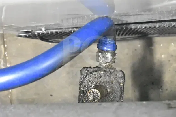 Close-up view of a gas connection for a commercial 8 burner range with evident grime, highlighting functional wear.
