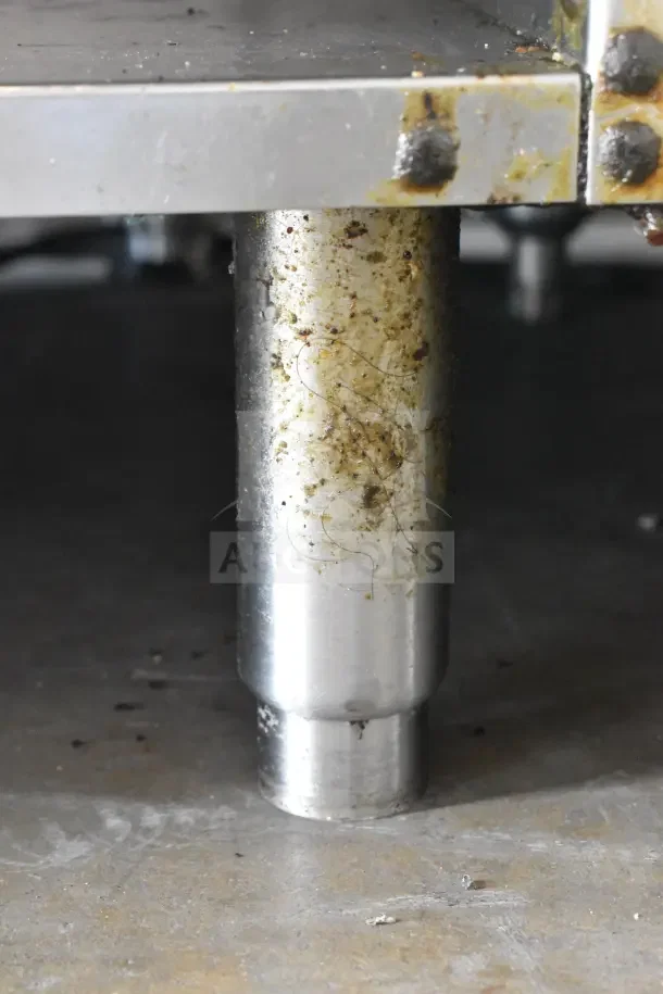 Close-up of the base and underside of a commercial 6 burner gas range, showing stainless steel construction and some surface stains.
