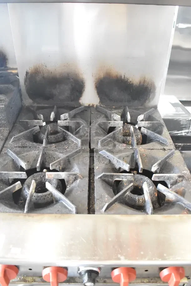Standex 24GFGV4B20N commercial range with 4 burners, oven, over shelf, and backsplash. Used condition, natural gas powered.
