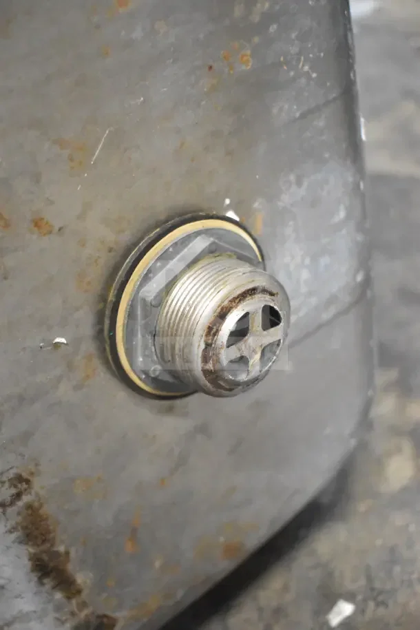 Close-up of the drain fitting of a commercial single bay sink, showing some rust and wear on the metal surface.