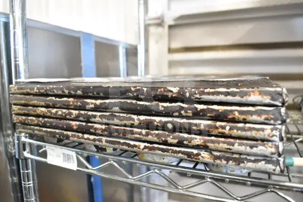 Five metal 24-cup muffin baking pans, well-used with visible wear, stacked on a metal shelf. Auction item tag visible.