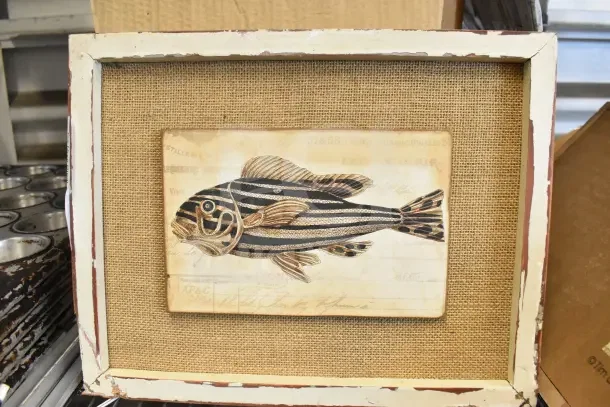 Rustic white frame with a fish illustration on burlap background, distressed edges, vintage condition.