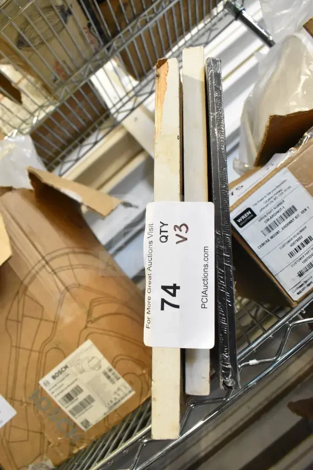 Three various frames including one with fish motifs, stacked in a storage area. Auction tag reads "74 QTY V3."