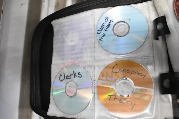 CD binder with contents, showing four discs labeled "Clerks," "Conspiracy Theory," and others, stored in a black case.
