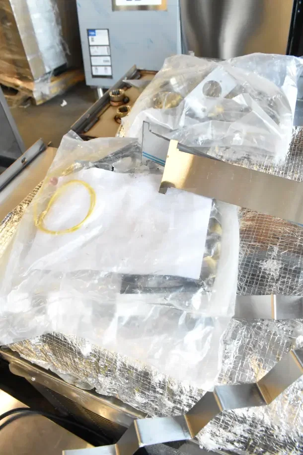 Metal unit packaged with protective wrap, featuring shiny components and fasteners. Appears new in packaging.