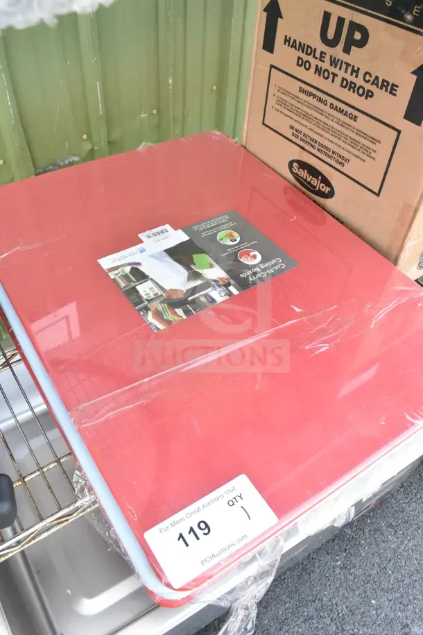 Brand new red cutting board, scratch and dent condition. Labeled "119" for auction with Salvajor shipping box nearby.