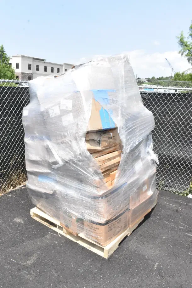 Clear plastic-wrapped pallet of assorted scratch and dent items including spoons, door, tumblers. Box labels visible.