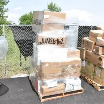Stack of boxes containing 36 new scratch and dent items, including plates and glasses, marked "JUN26-162," on a pallet.