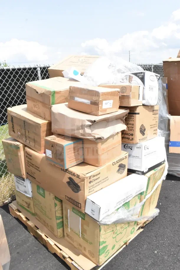 Stack of new scratch and dent items including hot cups and cutlery in assorted boxes on a pallet outdoors.