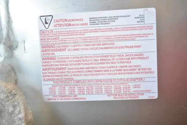 "Warning label on Amana RC17S2 Commercial Microwave Oven highlighting electrical shock hazards and compliance standards."