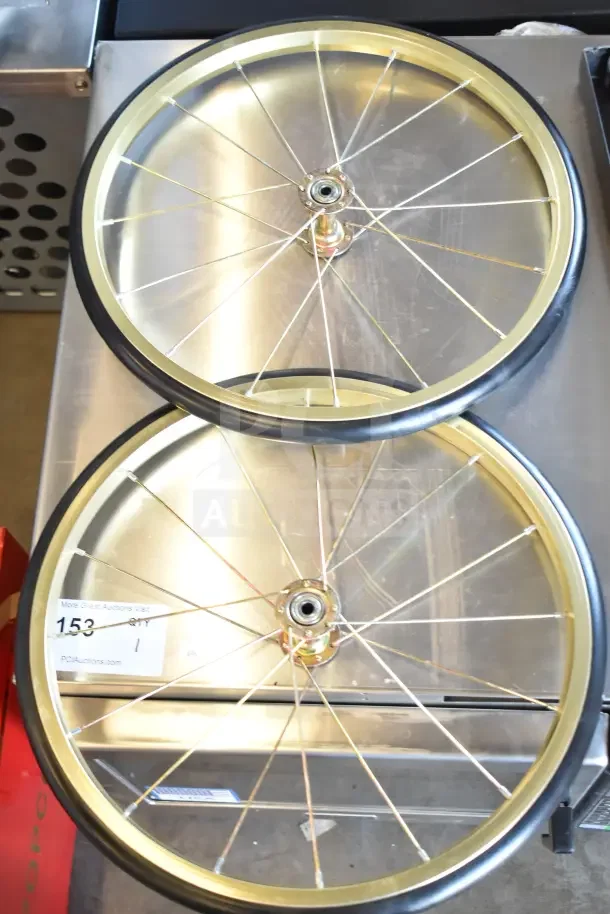 Golden wheels for a brand new scratch and dent popcorn cart, metal rims, rubber tires, with auction tag number 153 visible.