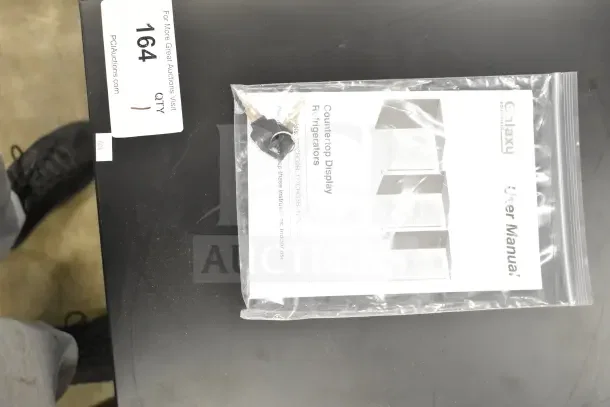 Brand new Galaxy 177CRG3B countertop display merchandiser user manual and keys in a plastic bag on a black surface.