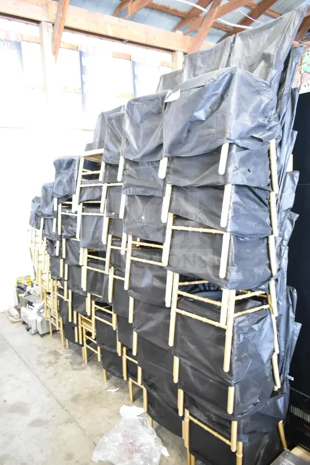 56 new Lancaster Table & Seating 164REINCHVRGLD gold Chiavari chairs, steel-reinforced, stacked with protective black covers.