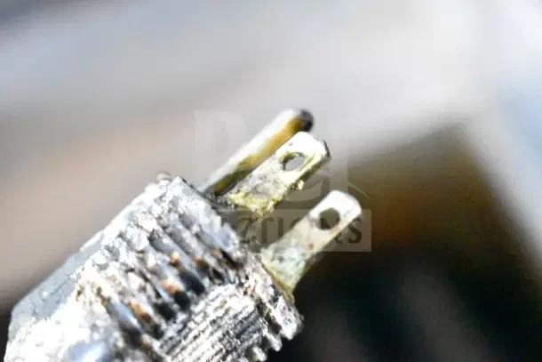 Close-up of a worn metal electrical plug with visible corrosion and discoloration.