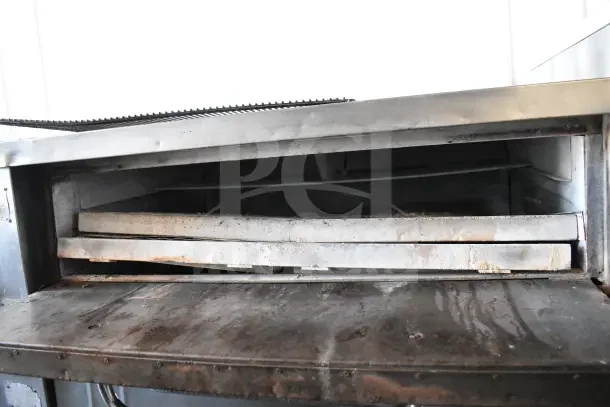 Bakers Pride gas-powered single deck pizza oven on metal legs, showing worn interior and exterior. Commercial use.