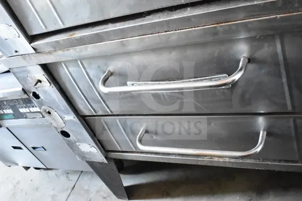 2 Bakers Pride gas-powered single deck pizza ovens on metal legs; stainless steel, used condition, sturdy handles.