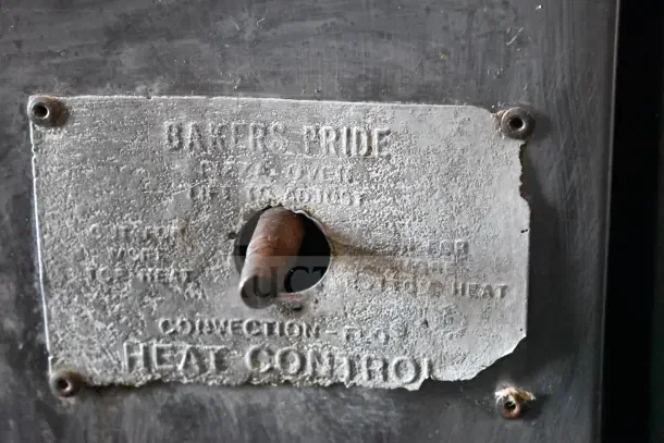 Aged label on a Bakers Pride commercial pizza oven, showing heat control settings and brand name.