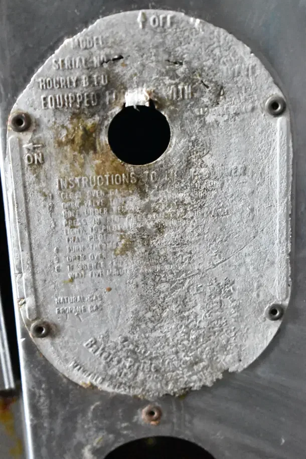 Bakers Pride gas pizza oven label, worn condition. Shows instructions and model details. Metal surface and screws visible.
