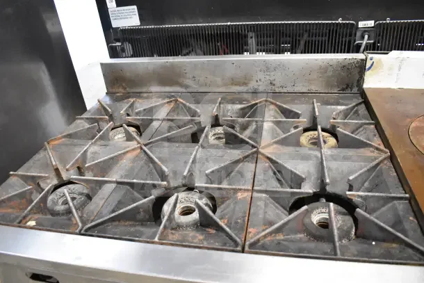 Vulcan Commercial 6-Burner Gas Range on countertop, signs of wear and rust, sturdy grates, industrial-grade cooking appliance.