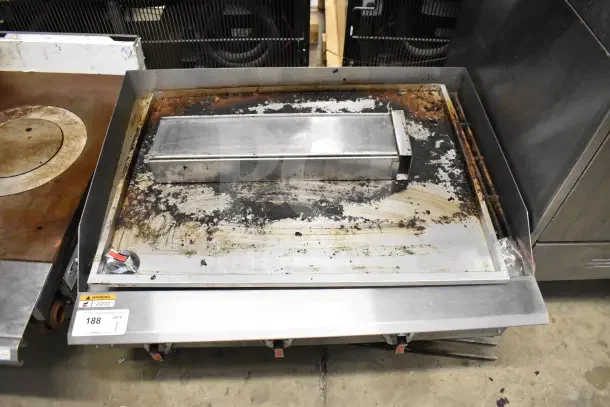 Commercial countertop gas-powered charbroiler grill with stainless steel construction, worn surface, and visible control knobs.