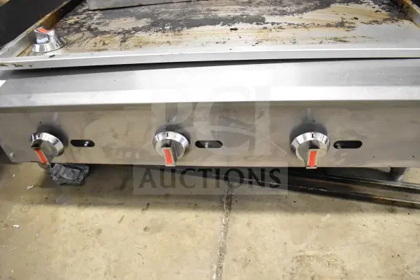 Commercial countertop gas charbroiler grill with three control knobs, stainless steel, used condition with visible wear.